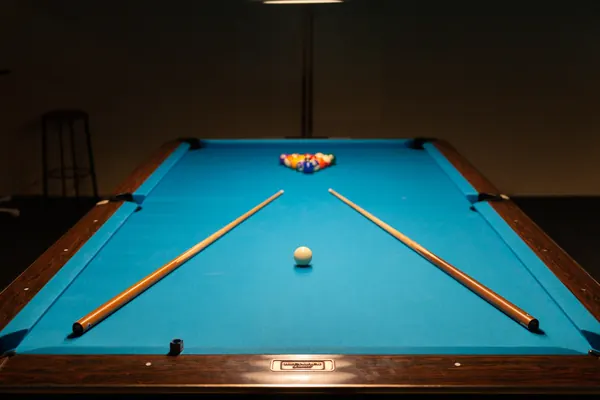 Billardtisch mit aufgebauten Kugeln im Dreieck und zwei Queues auf dem Tuch