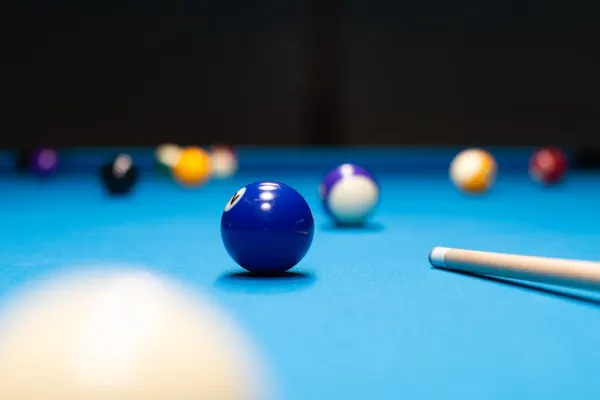Nahaufnahme einer blauen Billardkugel, dahinter weitere Kugeln und ein Queue