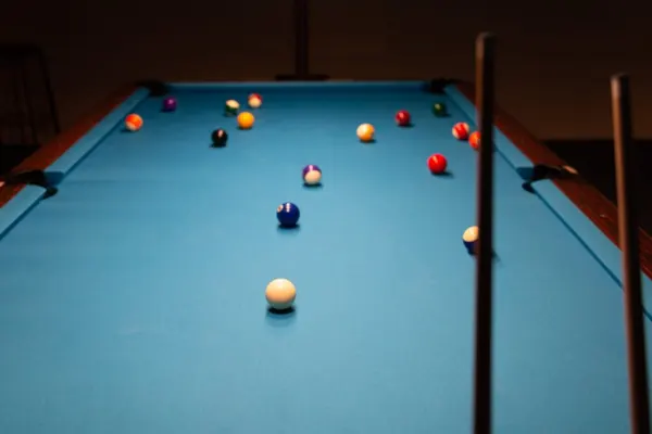 Billardkugeln verteilt auf blauem Tuch, rechts ein Queue