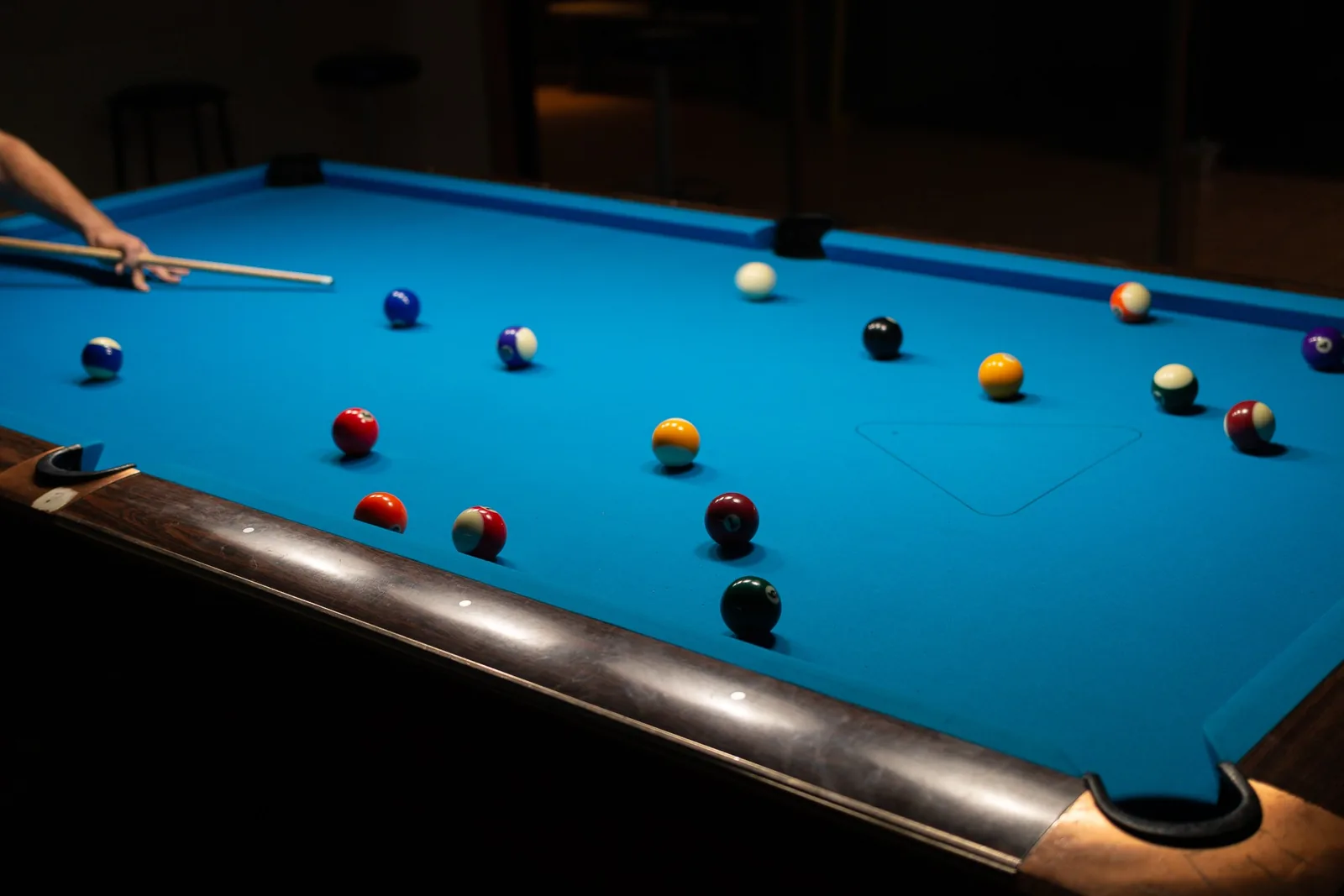 Spieler setzt am Pool-Billardtisch mit blauem Tuch zum Stoß an, die Kugeln liegen verteilt