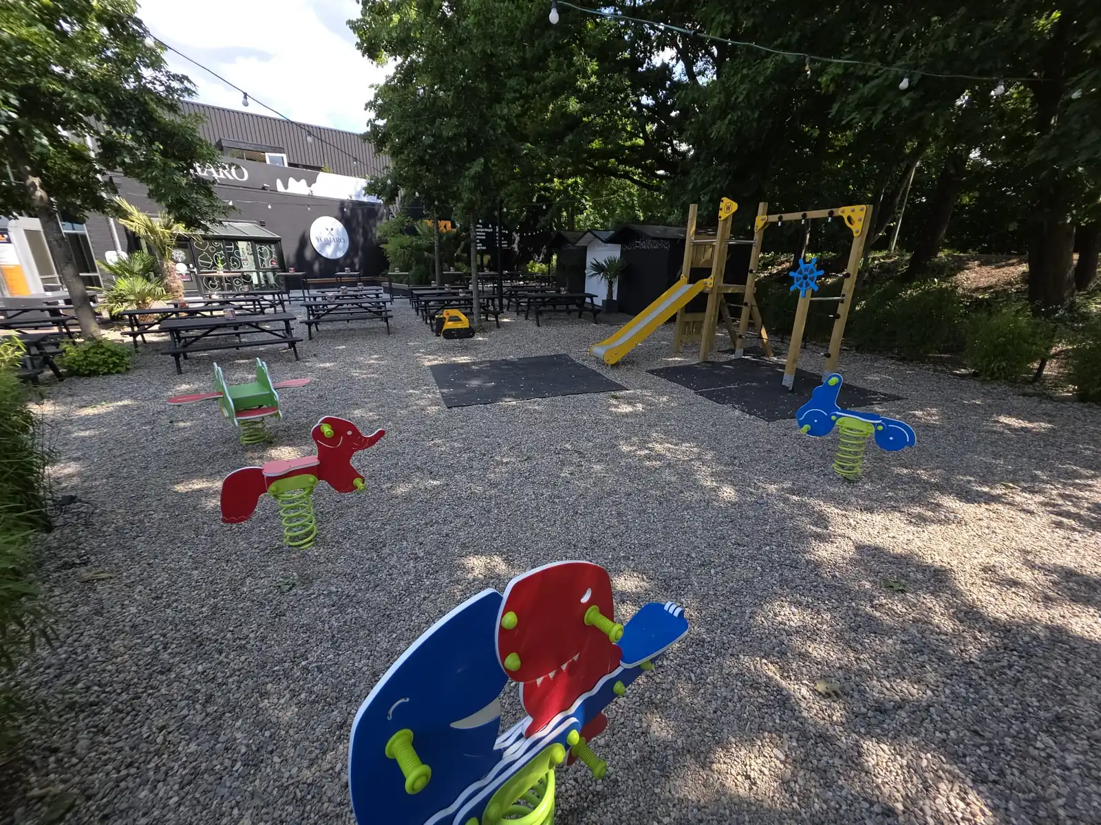 Spielplatz mit Rutsche und Wippgeräten unter Bäumen